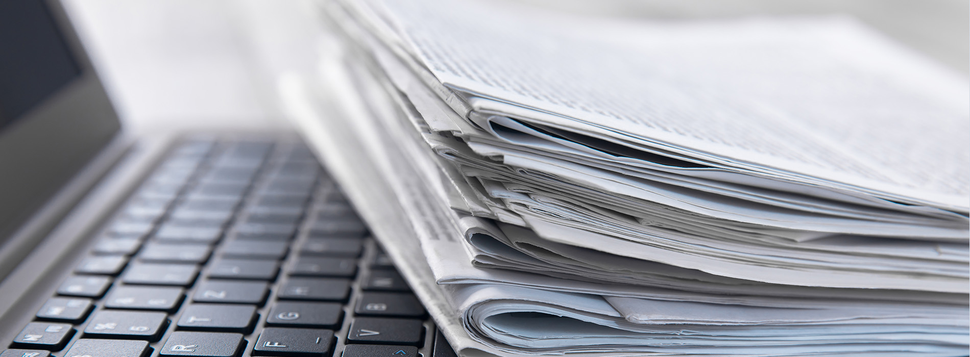 The image displays a stack of papers on top of a laptop keyboard, with the laptop partially visible at the bottom right corner.