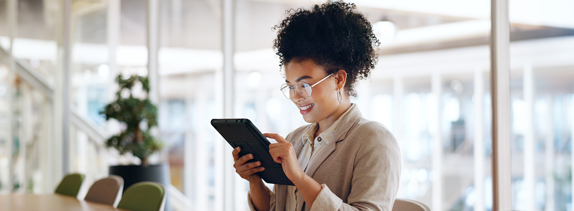 A person holding a tablet while standing in an indoor space with plants and modern decor.
