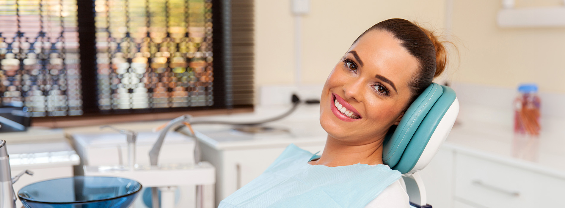 The image shows a woman sitting in a dental chair with a smile on her face, wearing a white headset and holding a microphone, likely indicating she is a dental professional or a patient receiving dental care.