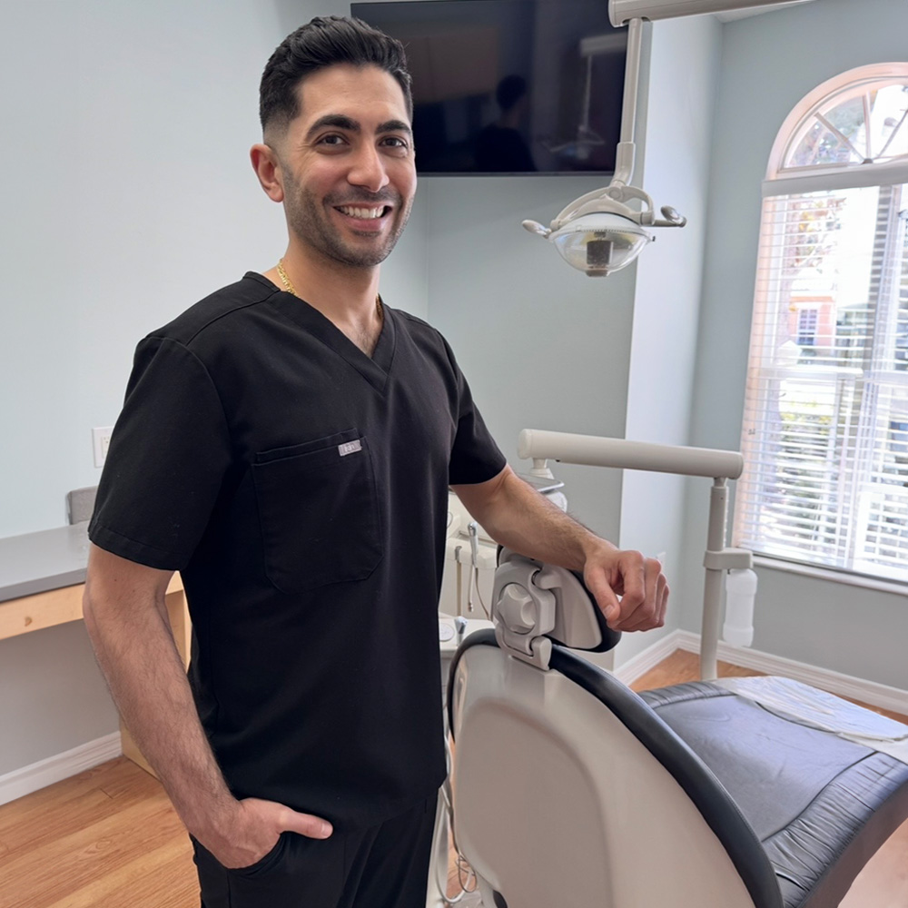 The image shows a woman sitting in a dental chair with her mouth open, receiving dental care from a professional who is cleaning her teeth using a dental tool.