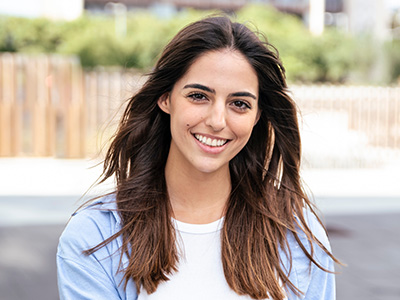 A young woman with long hair is smiling at the camera while posing outdoors.