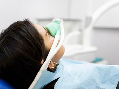 A person wearing a medical mask receiving oxygen therapy while lying on a dental chair with a medical device attached to their face.