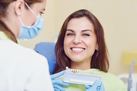 A woman receiving dental care from a professional, with the dentist holding up a dental tool, both wearing masks.