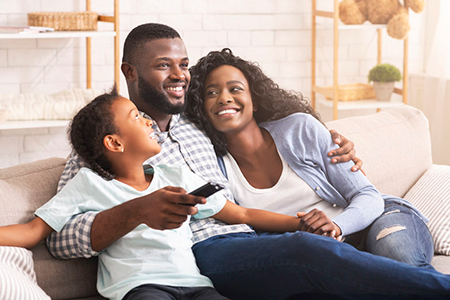 A family of four sitting on a couch with a man holding a remote control.