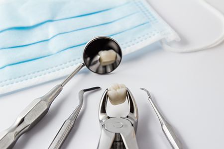 This image shows a collection of dental tools, including a toothbrush with toothpaste on its bristles, placed next to a blue surgical mask on a white surface.