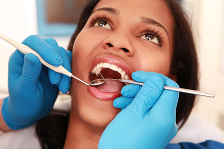 A woman receiving dental care with her mouth wide open, while a dentist works on her teeth using specialized tools.