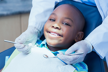 A young boy seated in a dental chair being attended to by a dentist, with both smiling.