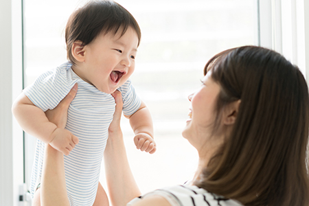 The image shows a smiling woman holding a baby with joyful expression, both indoors with natural light illuminating them.