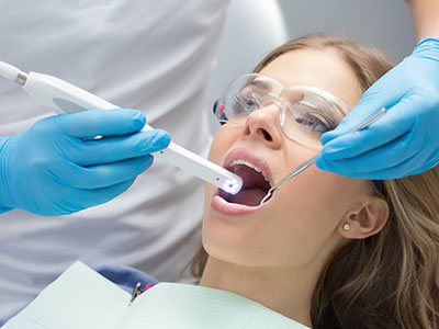 A woman receiving dental treatment with a device held by a dental professional.